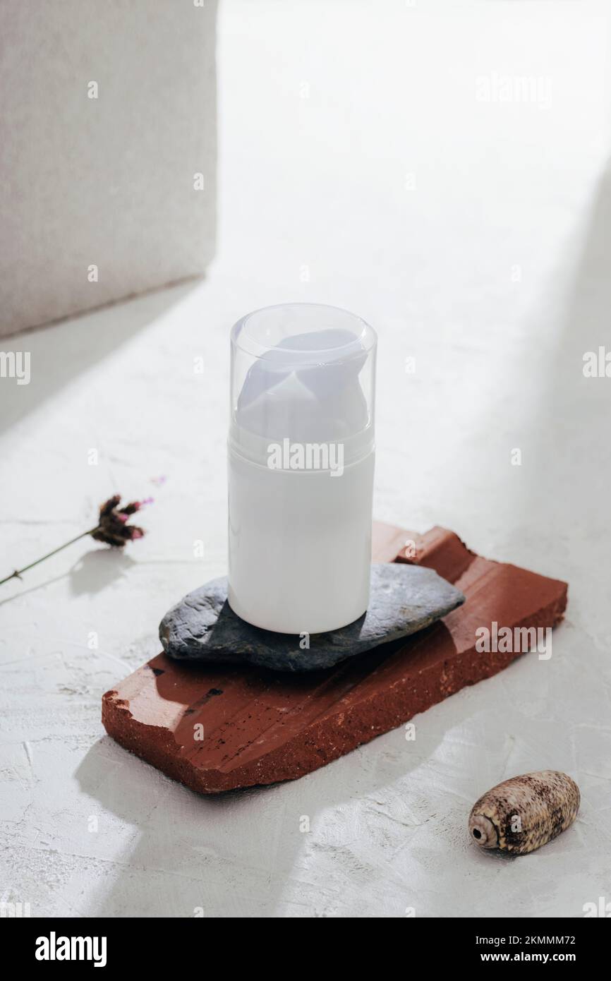 Bouteille cosmétique blanche sur le podium en pierres naturelles au soleil. Cosmétiques naturels, spa et concept de bien-être, maquette. Banque D'Images