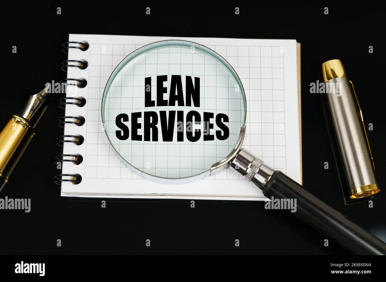 Concept commercial et financier. Sur une surface noire, il y a un stylo, un bloc-notes et une loupe. L'inscription dans le carnet - LEAN SERVICES Banque D'Images