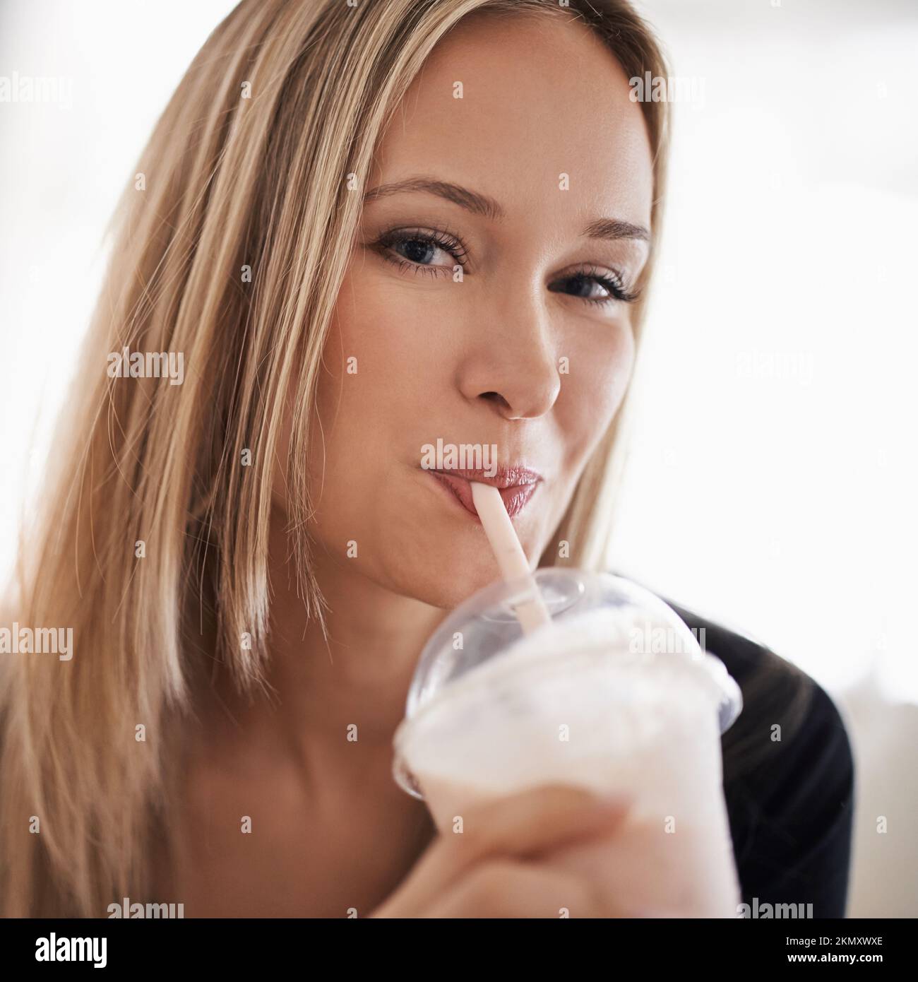 Sirotez quelque chose de sucré. Portrait d'une jeune femme buvant un milk-shake à la maison. Banque D'Images