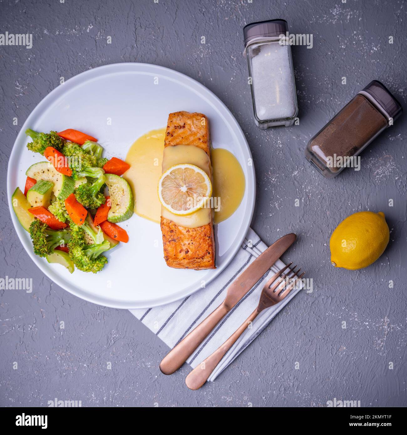 Vue de dessus d'un saumon cuit couvert de sauce crémeuse avec légumes sautés dans une assiette blanche Banque D'Images