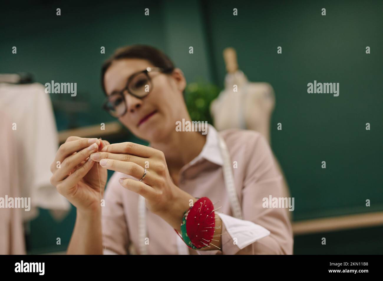 Femme asiatique designer filetage de l'aiguille. Femme designer de mode travaillant dans son studio avec foyer dans les mains de mettre le fil dans l'aiguille de couture. Banque D'Images
