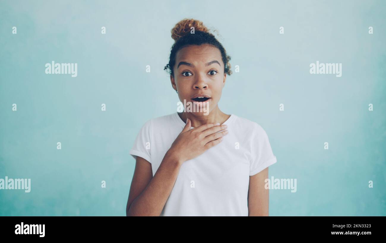 Portrait d'une femme afro-américaine surprise qui lève les sourcils et qui couvre sa bouche ouverte avec la main exprimant l'étonnement puis souriant. Bonnes nouvelles et concept de personnes. Banque D'Images