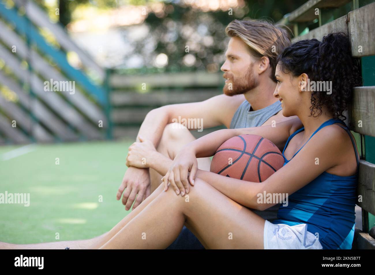 jeune couple assis avec un ballon sur le terrain de basket-ball Banque D'Images