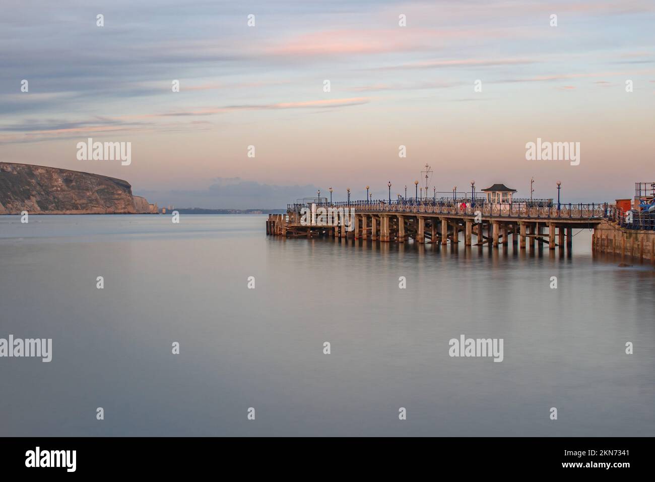 Une longue exposition claire en novembre soir regardant à travers les eaux lisses et vides le long de Swanage Pier avec un ciel rose Banque D'Images