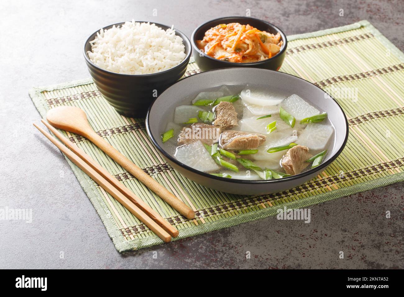 La soupe sud-coréenne nourrissante et légère de muguk combine des morceaux de bœuf et des tranches de radis coréens mu servis avec du riz et des kimchi sur le tapis du Banque D'Images