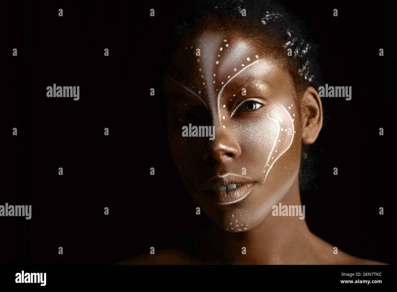 Portrait d'une belle fille africaine avec des peintures tribales traditionnelles sur son visage sur fond noir Banque D'Images