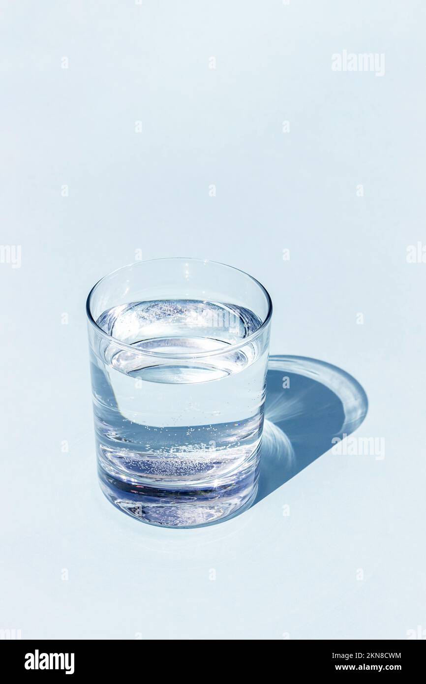 Un verre d'eau bleu avec une forte ombre nette sur fond bleu avec espace de copie. Banque D'Images