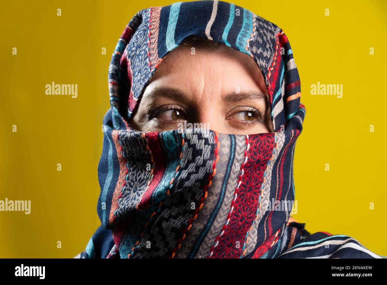 Portrait rapproché d'une femme portant le hijab, regardant sur le côté, isolée sur fond jaune de studio. Banque D'Images