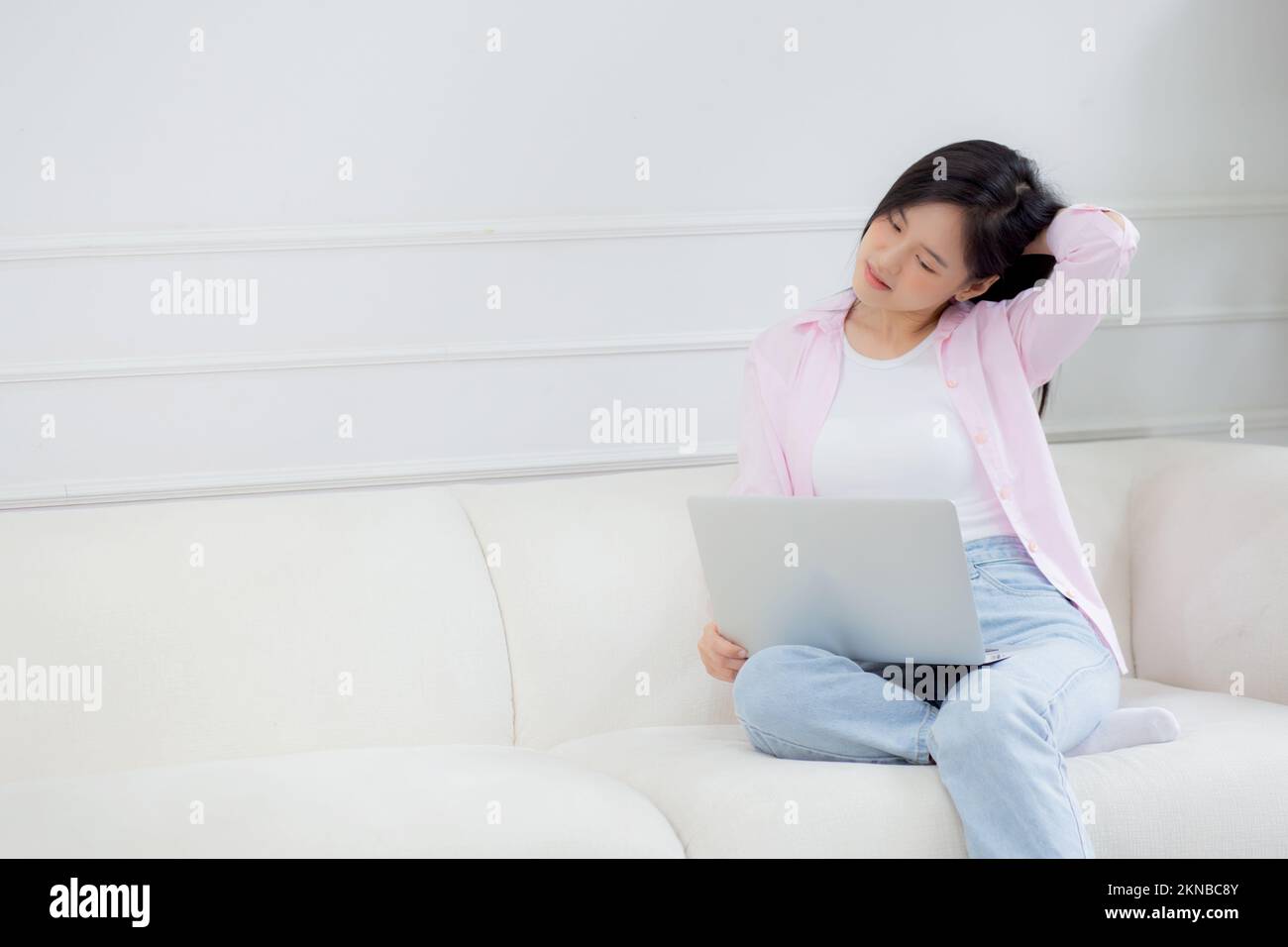 Belle jeune femme d'affaires asiatique assise sur un canapé et travaillant de la maison et de se détendre tout en étirant le cou de muscle pour se détendre dans le salon à la maison, femme Banque D'Images