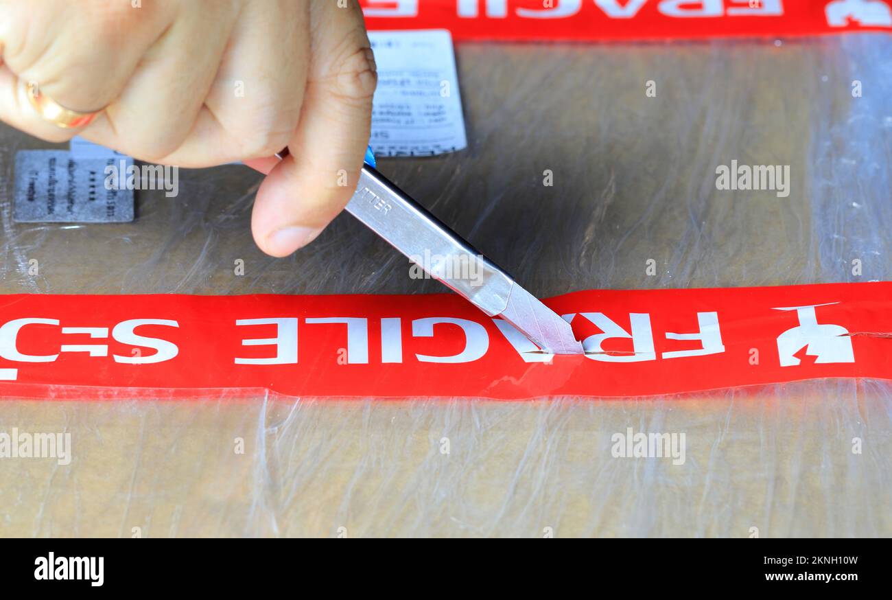 Ouverture à droite d'une boîte avec étiquette fragile à l'aide d'un petit couteau. Banque D'Images