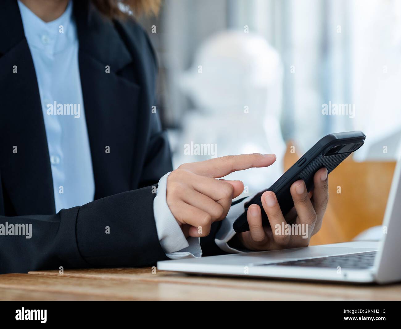 Le doigt de la femme d'affaires se touchant sur le téléphone portable. Téléphone portable intelligent noir dans la main de la personne près de l'ordinateur portable sur le bureau. Cyber-securi Banque D'Images