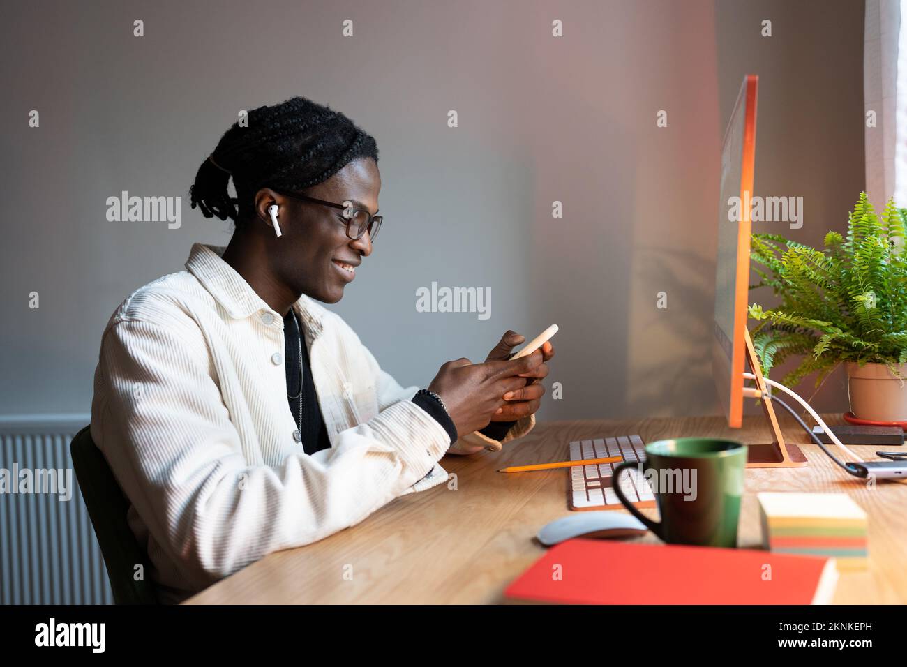 Jeune étudiant africain utilisant un smartphone, bavardant avec des amis tout en étudiant en ligne à la maison Banque D'Images