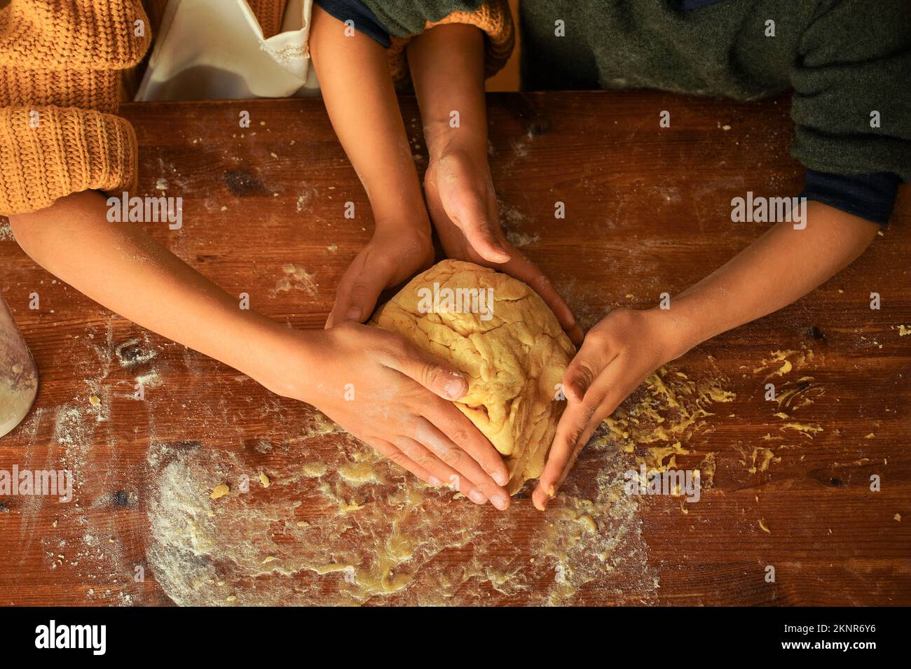 Les enfants pétrissent la pâte à biscuits avec leurs mains sur une table en bois. Banque D'Images