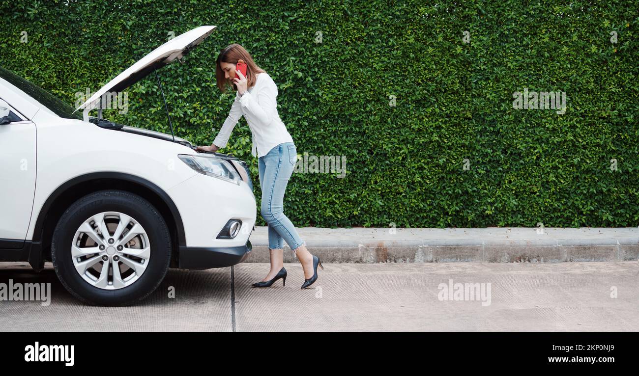 Une jeune femme dans une voiture a fait une panne sur la route pour tenter de résoudre le problème et a appelé un atelier de réparation de voiture ou quelqu'un près de l'aide. Banque D'Images