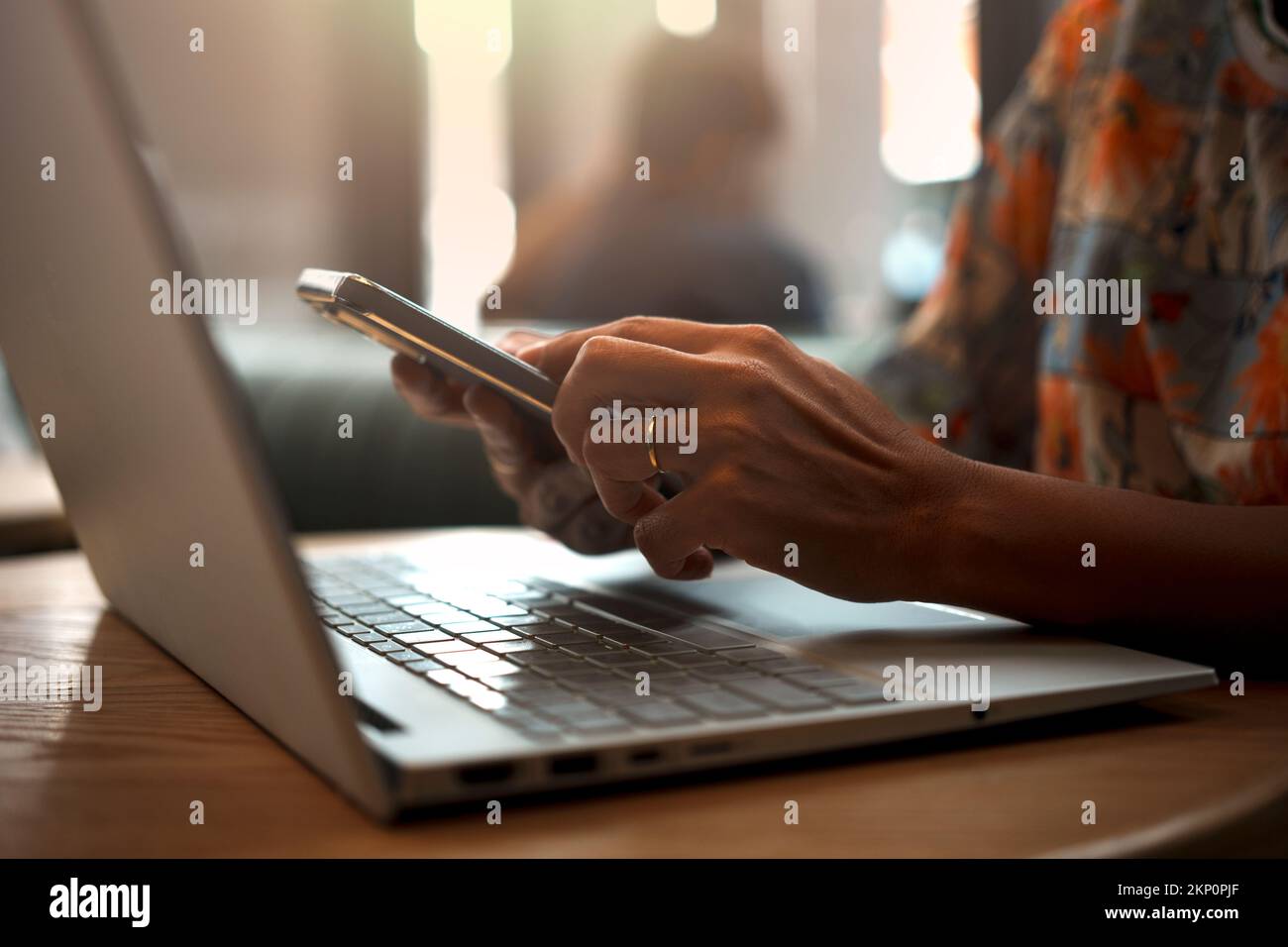 Gros plan de la main d'une femme utilisant un smartphone tout en travaillant sur un ordinateur portable dans un café. Banque D'Images