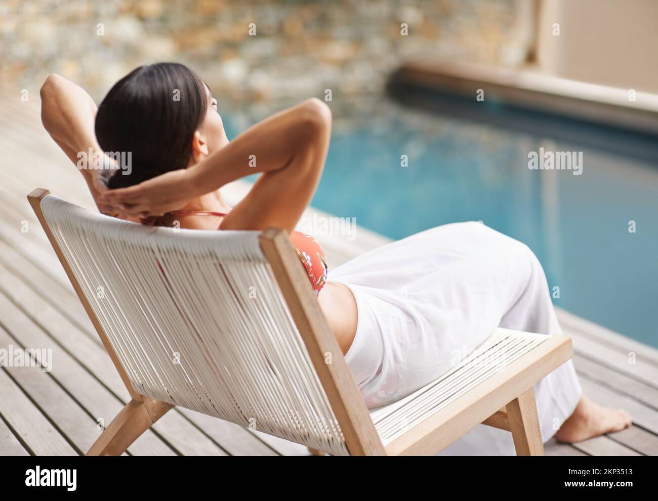 Ce n'est pas la vie... vue arrière d'une jeune femme qui se détend sur une chaise longue au bord de la piscine. Banque D'Images