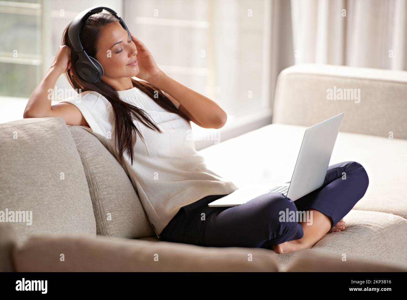 Des morceaux qui me racontent. Une jeune femme attirante qui écoute de la musique tout en utilisant son ordinateur portable à la maison. Banque D'Images