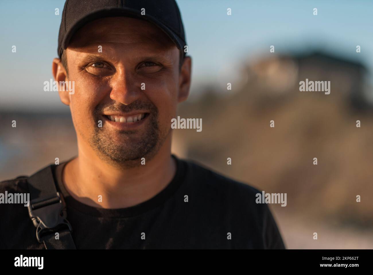 Un beau brunette dans un t-shirt noir sourit et regarde la caméra sur fond de montagnes et de ciel bleu. Photo de haute qualité. Banque D'Images