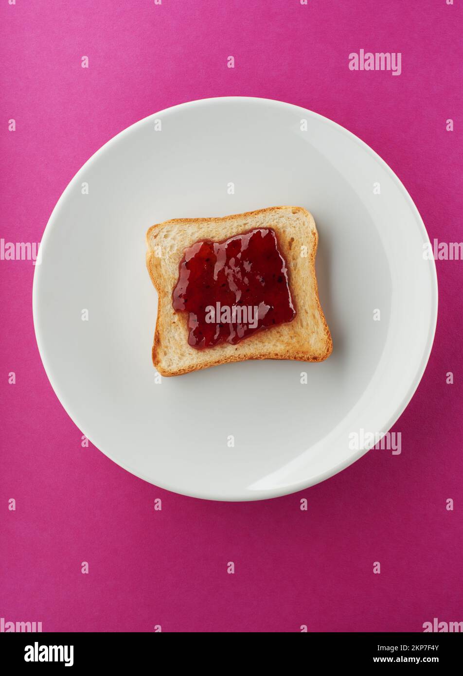 Tranche de pain grillé croustillante avec confiture de fraise sur plaque blanche et fond rose vif Banque D'Images