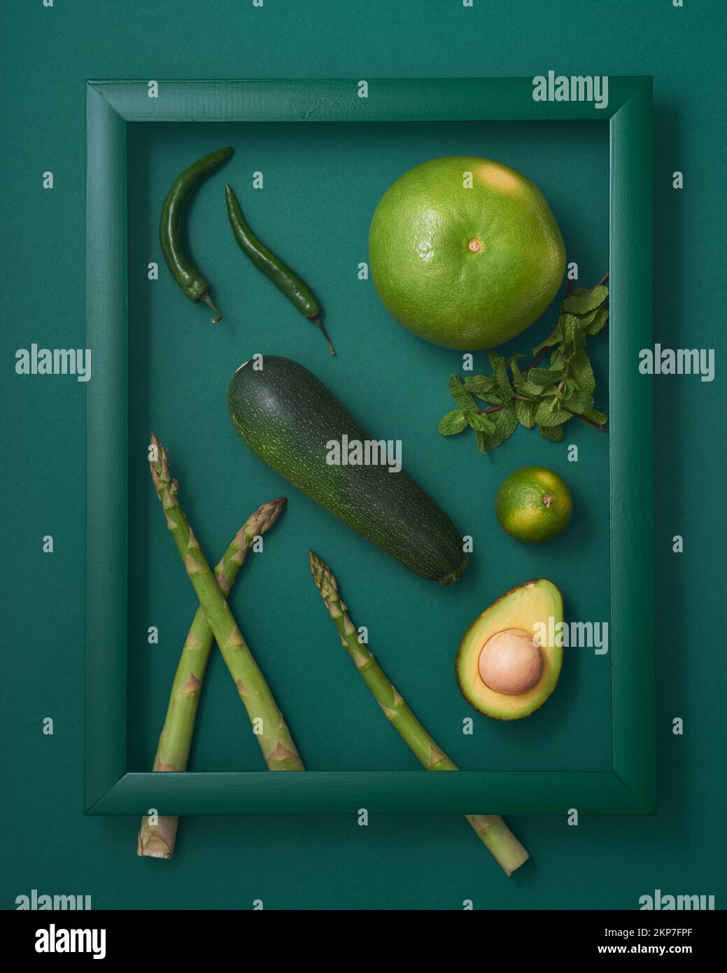 Courgettes, asperges, piment, avocat, lime, pomelo et menthe dans cadre en bois sur fond vert Banque D'Images