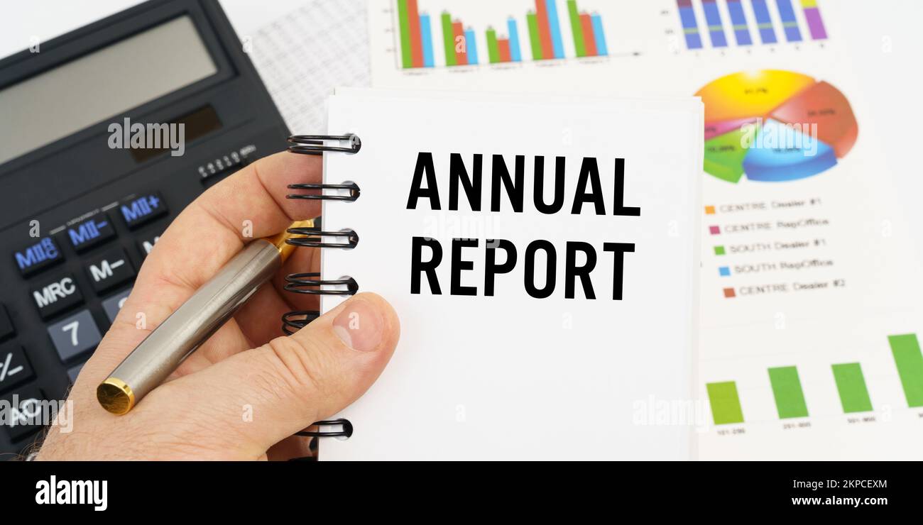 Concept de finance et d'économie. L'homme tient un stylo et un carnet avec l'inscription - RAPPORT ANNUEL. En arrière-plan sont des tableaux financiers, c Banque D'Images