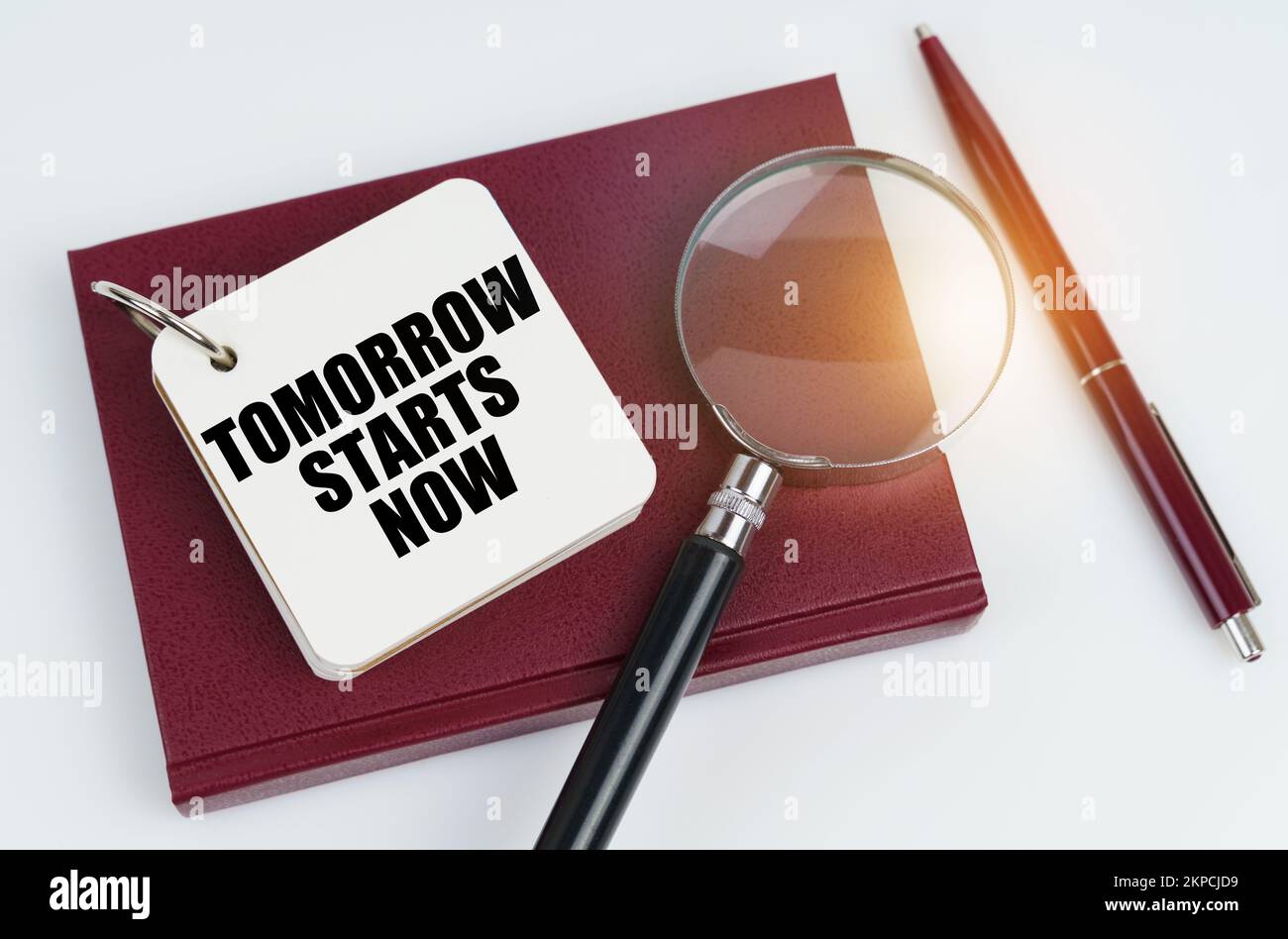 Concept commercial et financier. Sur une surface blanche se trouve un carnet rouge et un stylo, dans le carnet blanc l'inscription - DEMAIN COMMENCE MAINTENANT Banque D'Images