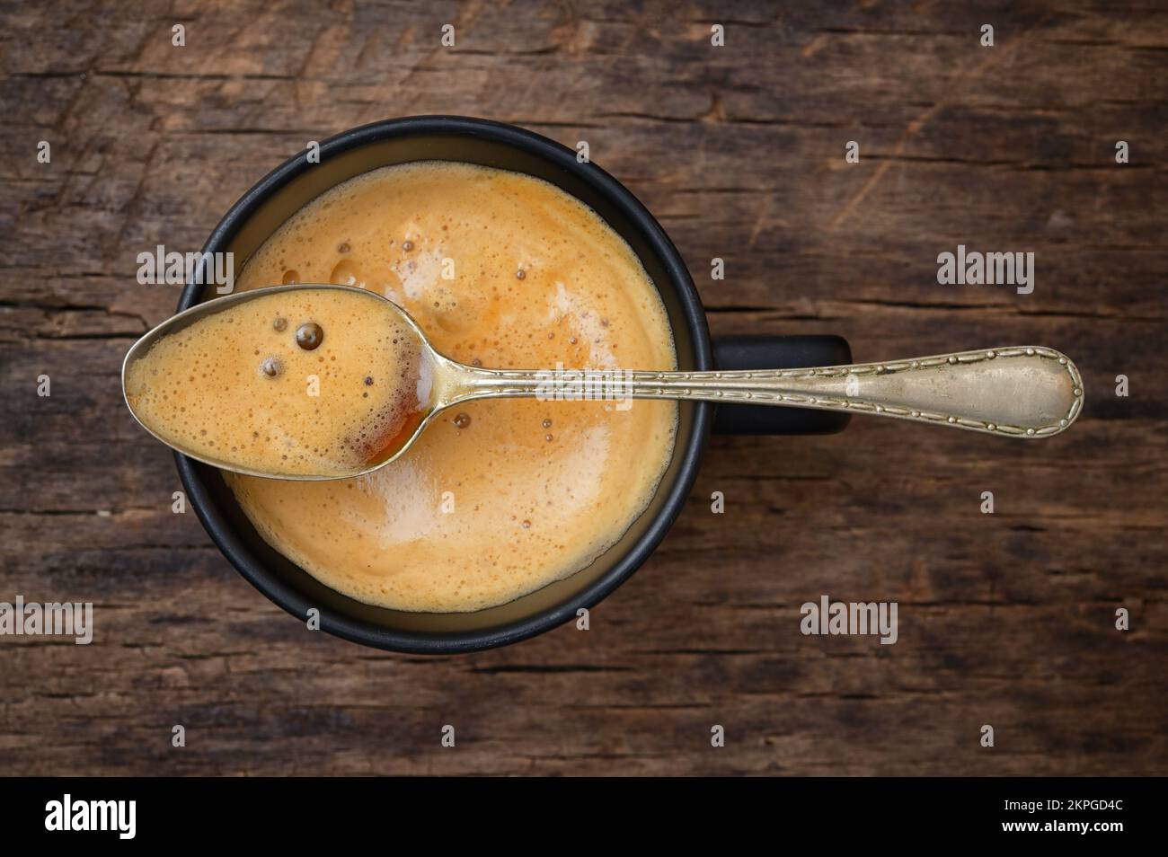 Tasse à espresso et cuillère noires avec mousse sur table en bois Banque D'Images