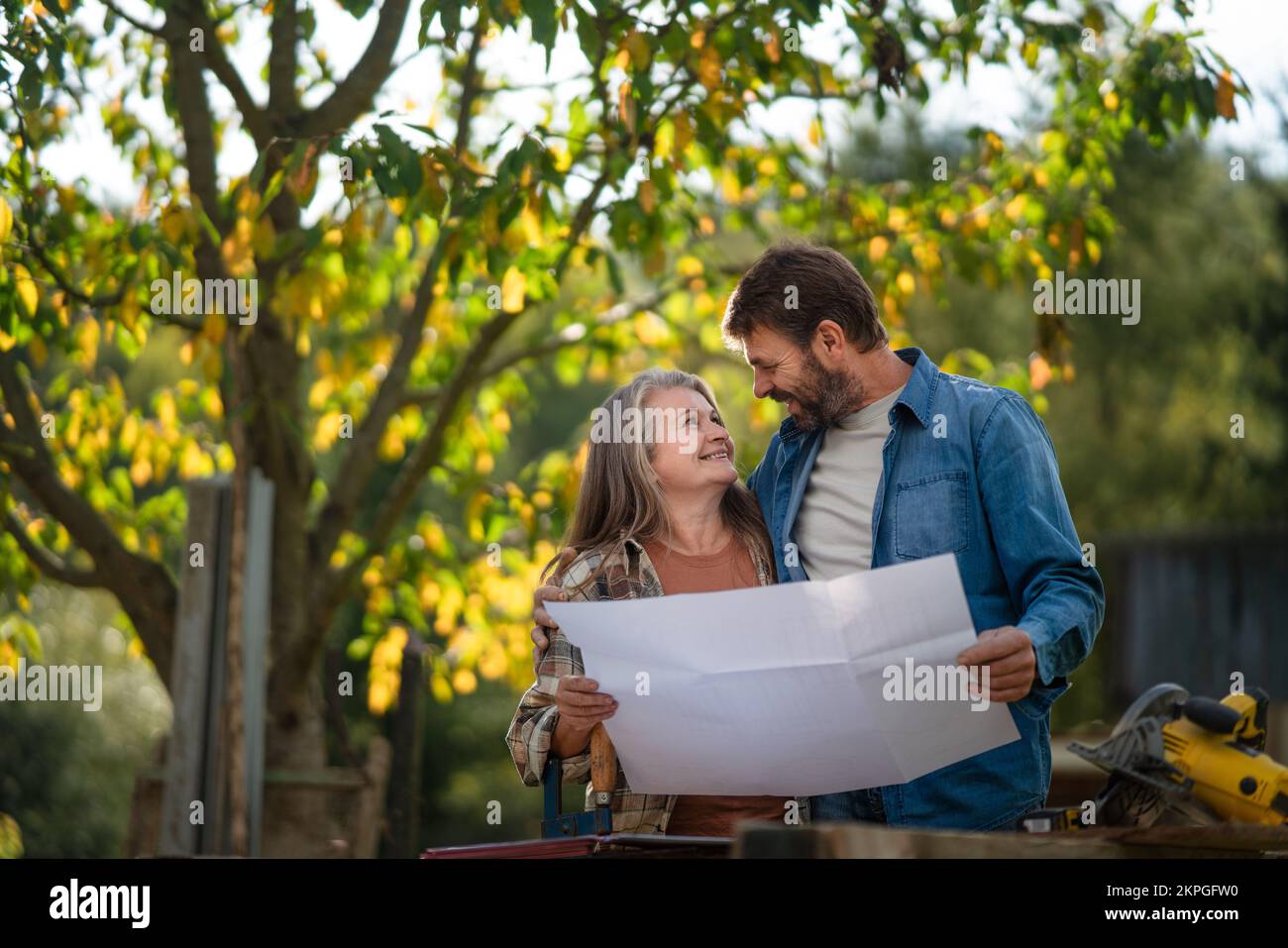 Heureux couple mature avec des plans architecturaux de leur future maison, debout à l'extérieur. Banque D'Images