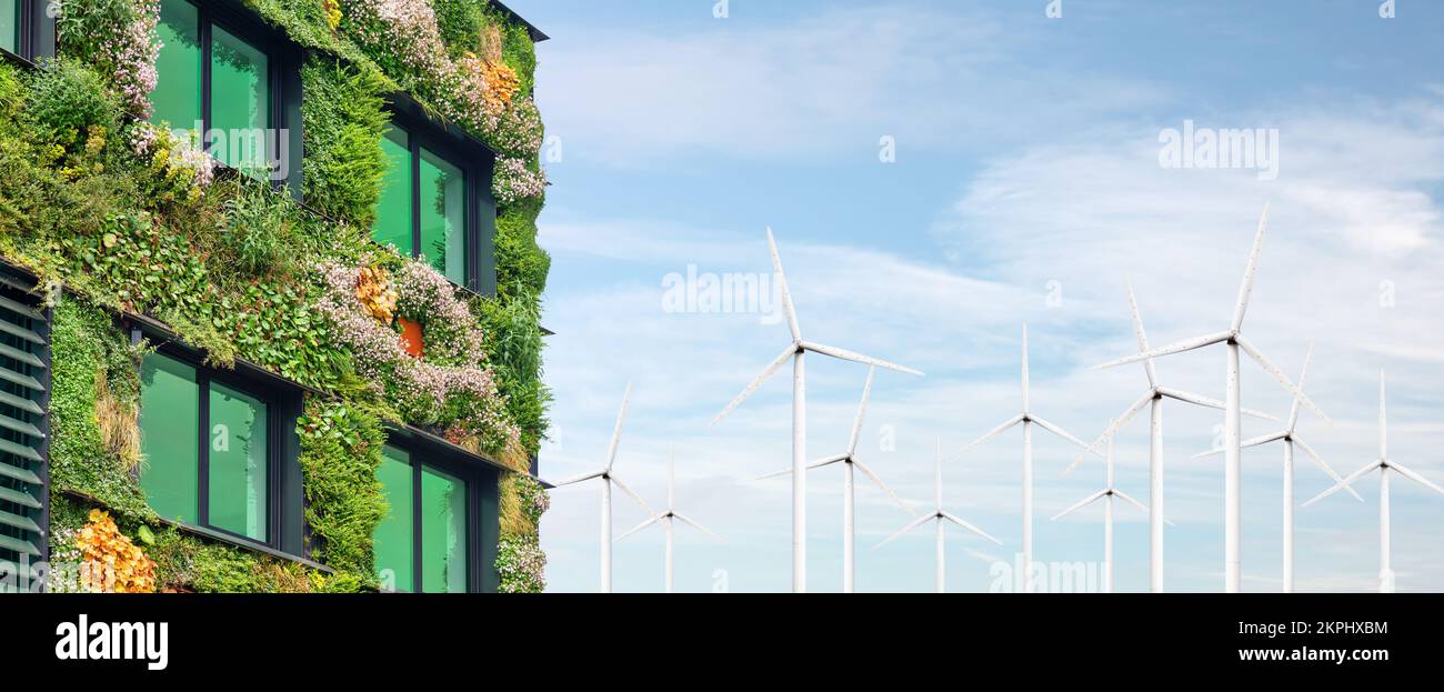 Extérieur d'un bâtiment vert durable recouvert de plantes suspendues verticales en fleurs devant des éoliennes Banque D'Images