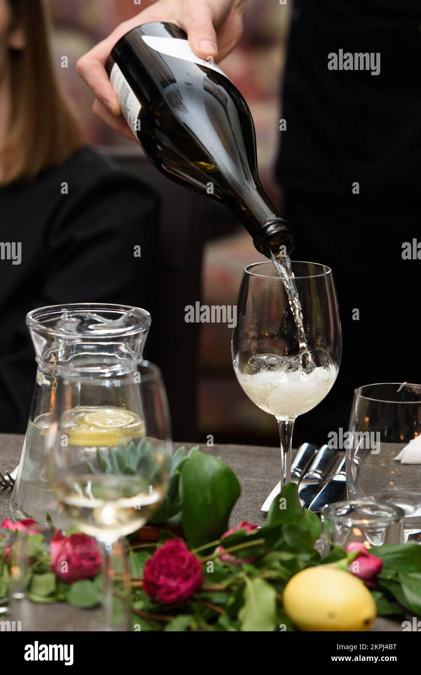 Un serveur verse du vin blanc dans un verre à une table de restaurant Banque D'Images