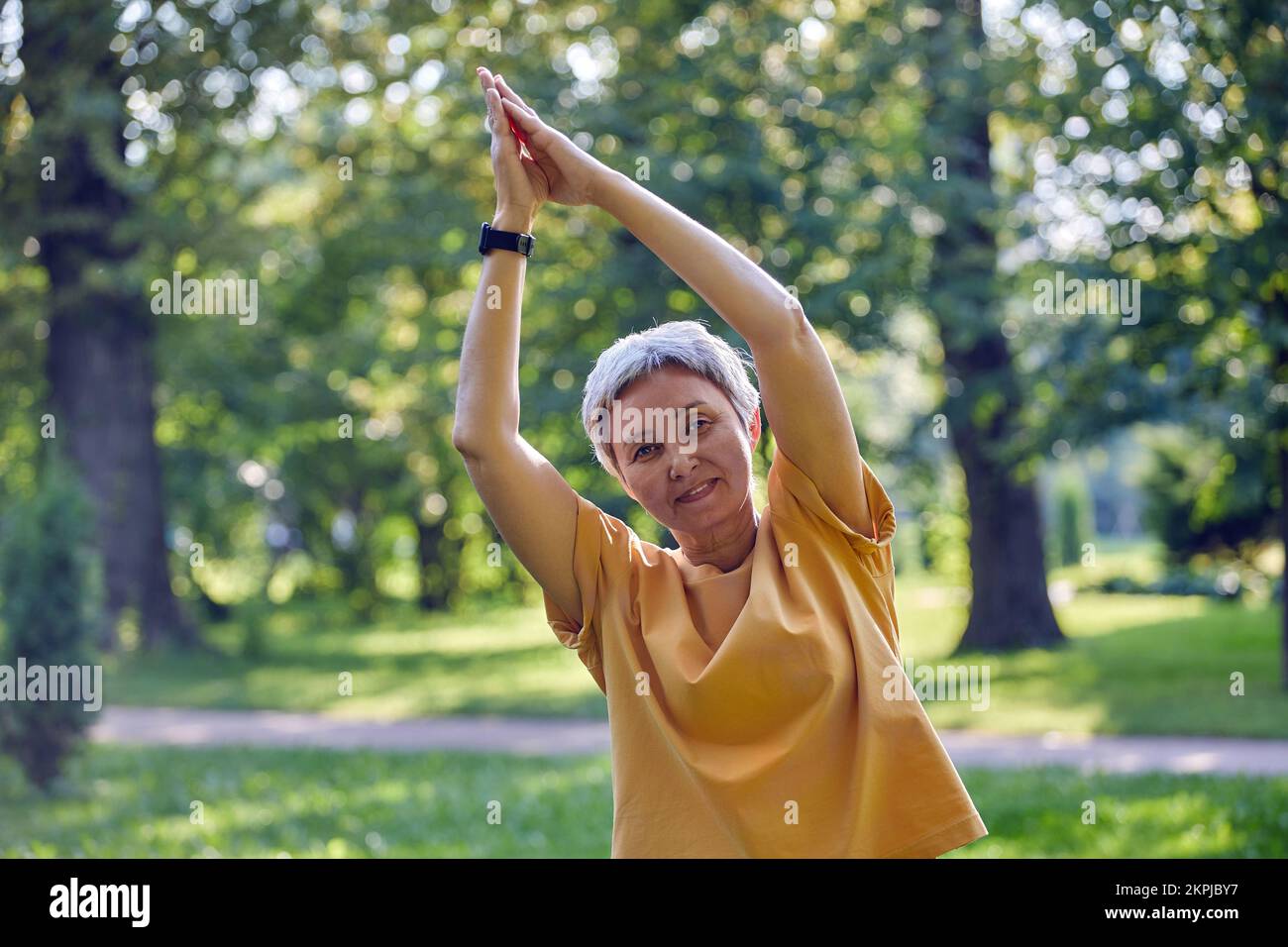 Femme asiatique active plus âgée dans les vêtements de sport regarde la caméra méditant dans le parc d'été avec des paumes repliées fait des exercices d'étirement, faire de l'exercice de yoga Banque D'Images