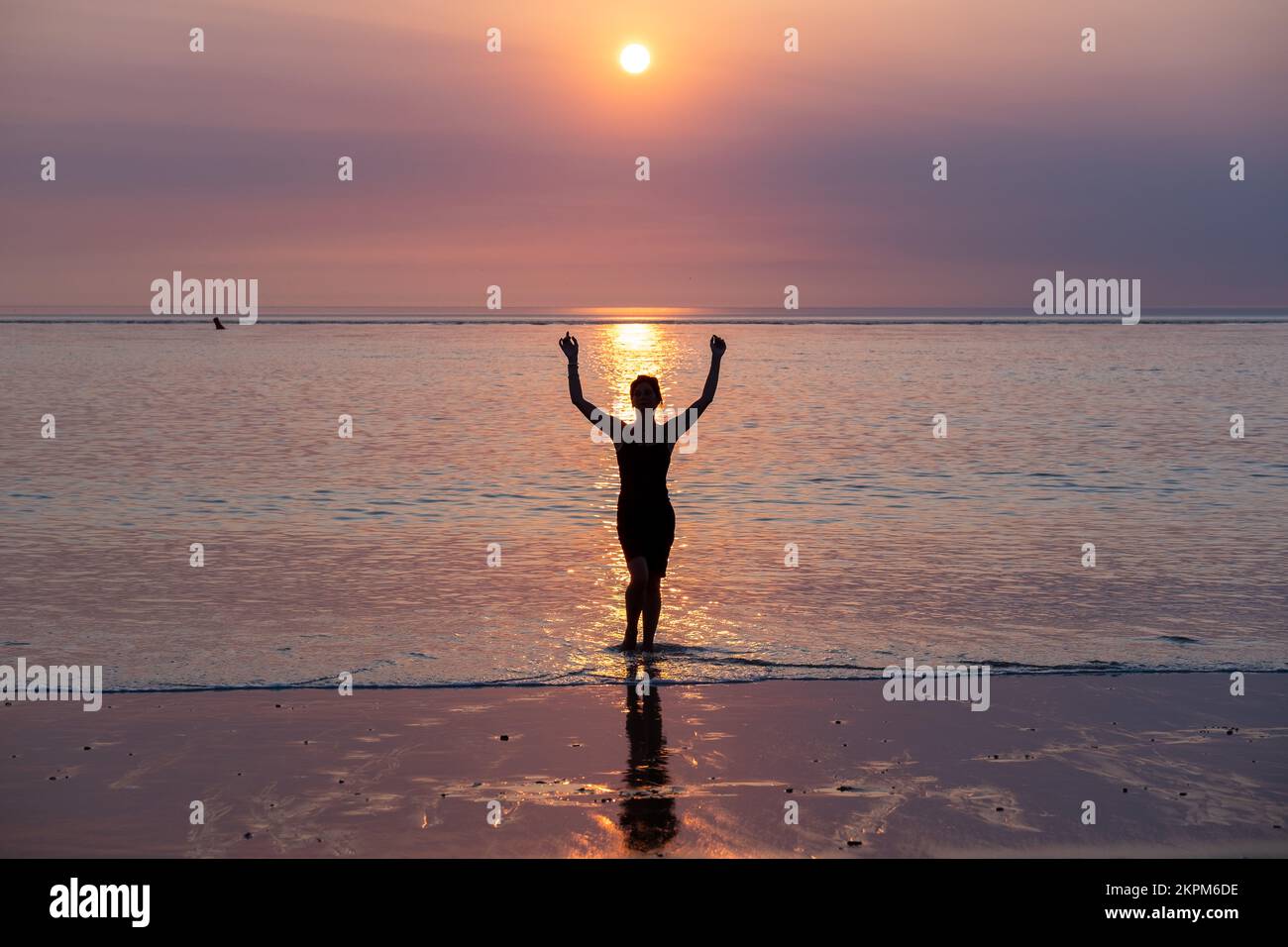 Silhouette d'une femme debout au fond de la cheville en mer avec ses bras dans l'air au coucher du soleil, France Banque D'Images