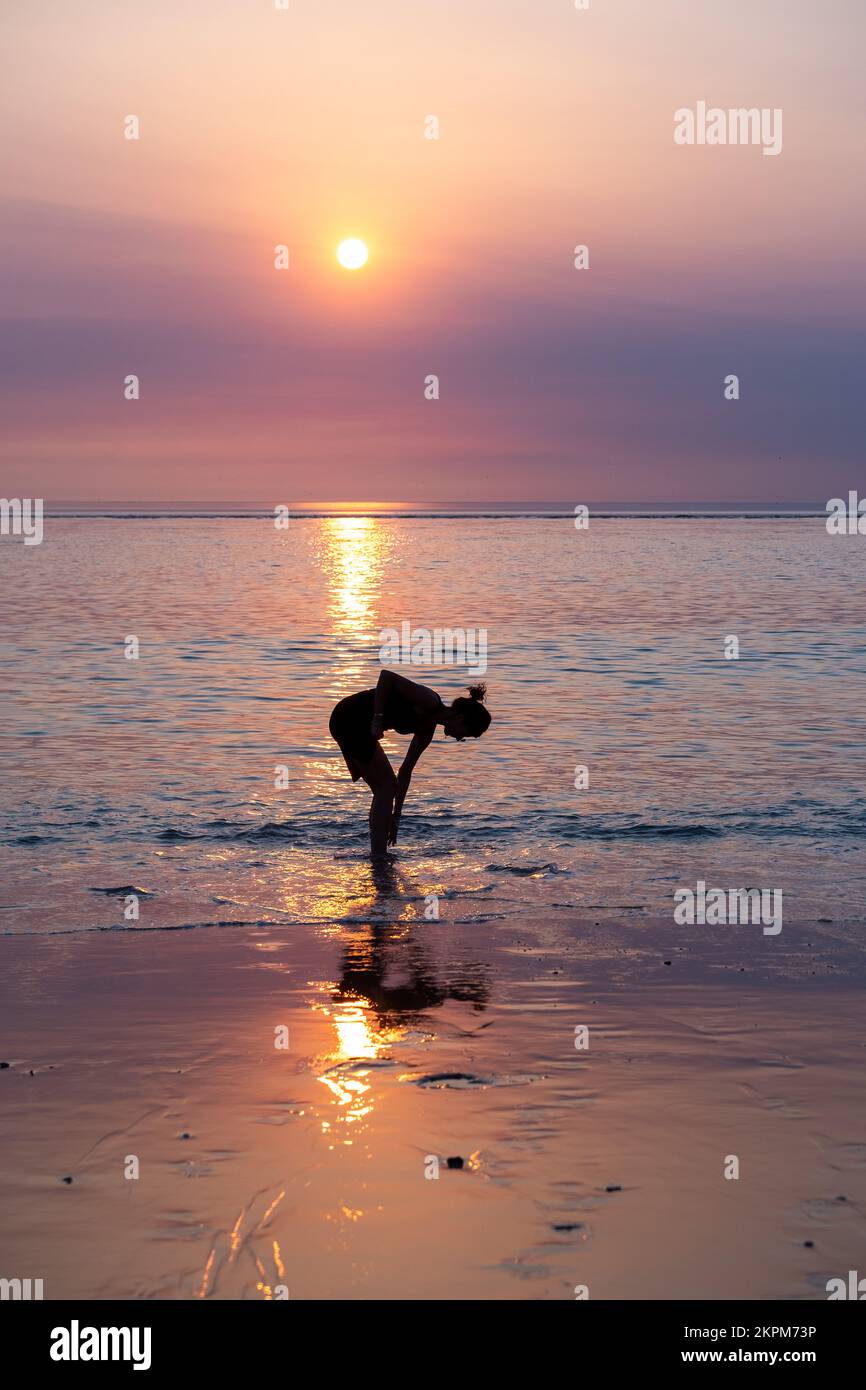 Silhouette d'une femme debout au fond de la cheville dans l'eau de mer éclaboussant sur ses jambes, France Banque D'Images