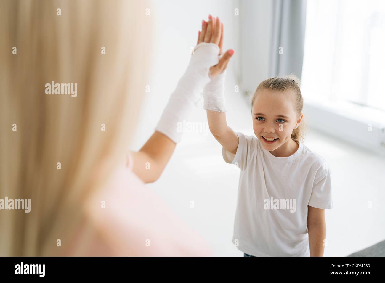 Vue rapprochée en grand angle de la jeune femme blonde blessée et de la petite fille avec une main cassée enveloppée dans un bandage en plâtre donnant cinq hauts Banque D'Images
