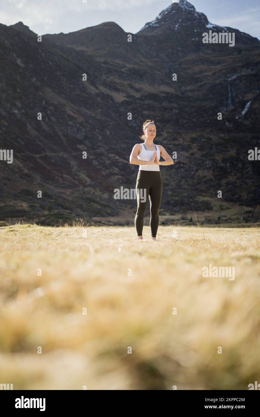 Femme sereine faisant du yoga dans une prairie alpine avec ses mains dans la pose de prière, Gastein, Autriche Banque D'Images