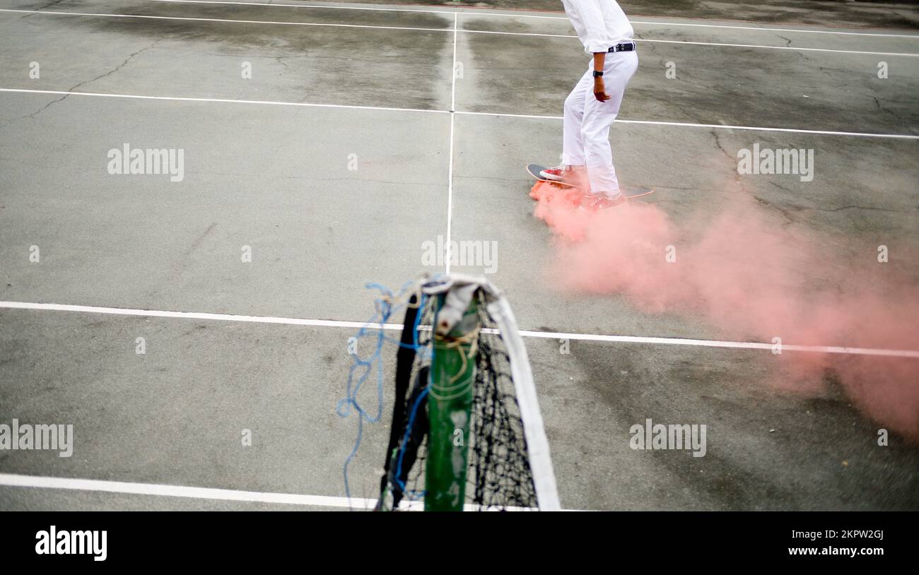 Blanc uniforme étudiant jouant à la planche à roulettes trick avec la fumée rose sur le skateboard Banque D'Images