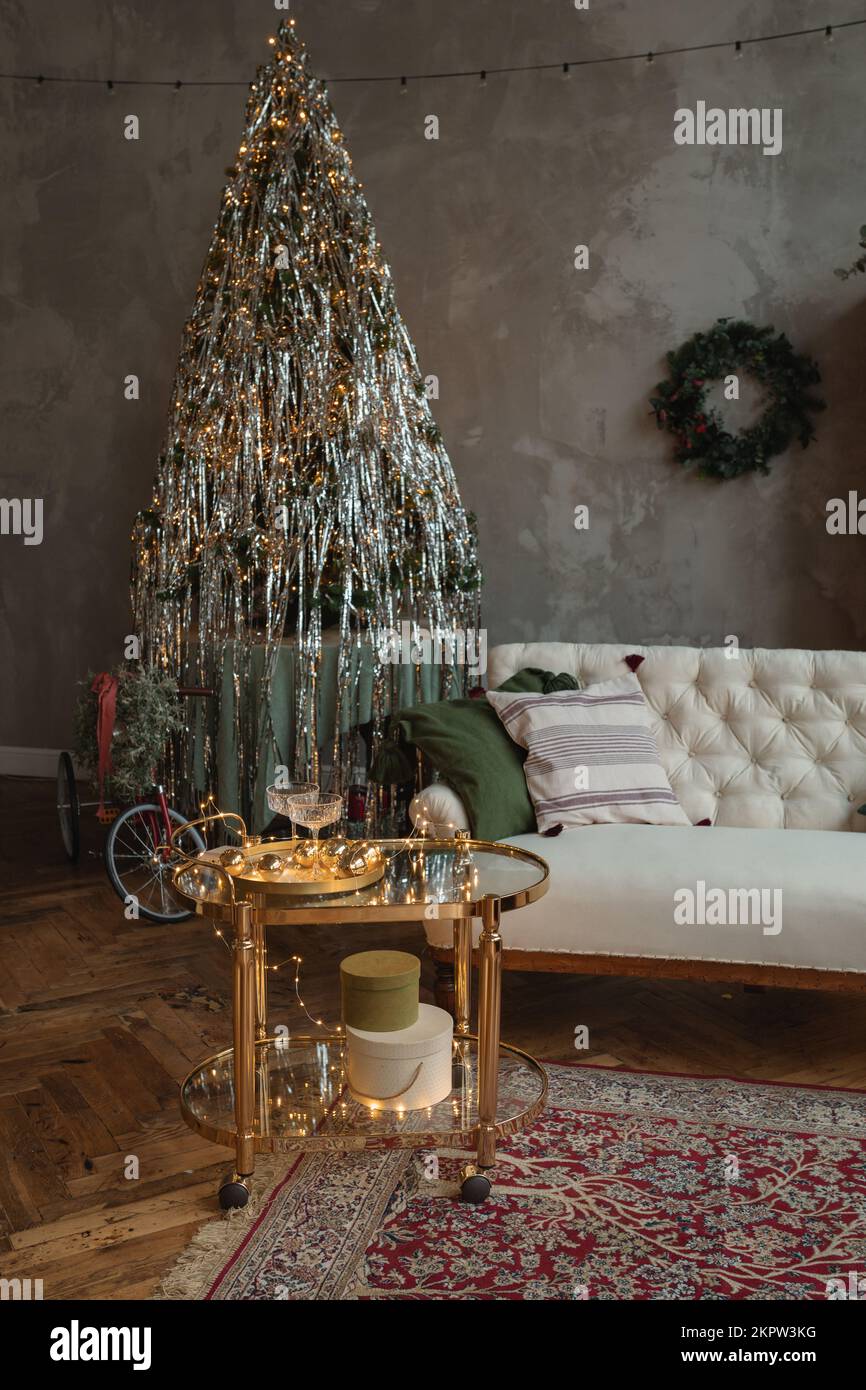 Vélo enveloppé d'un arc à côté d'un sapin de Noël dans un salon avec un canapé et une table latérale décorée de lumières de Noël Banque D'Images