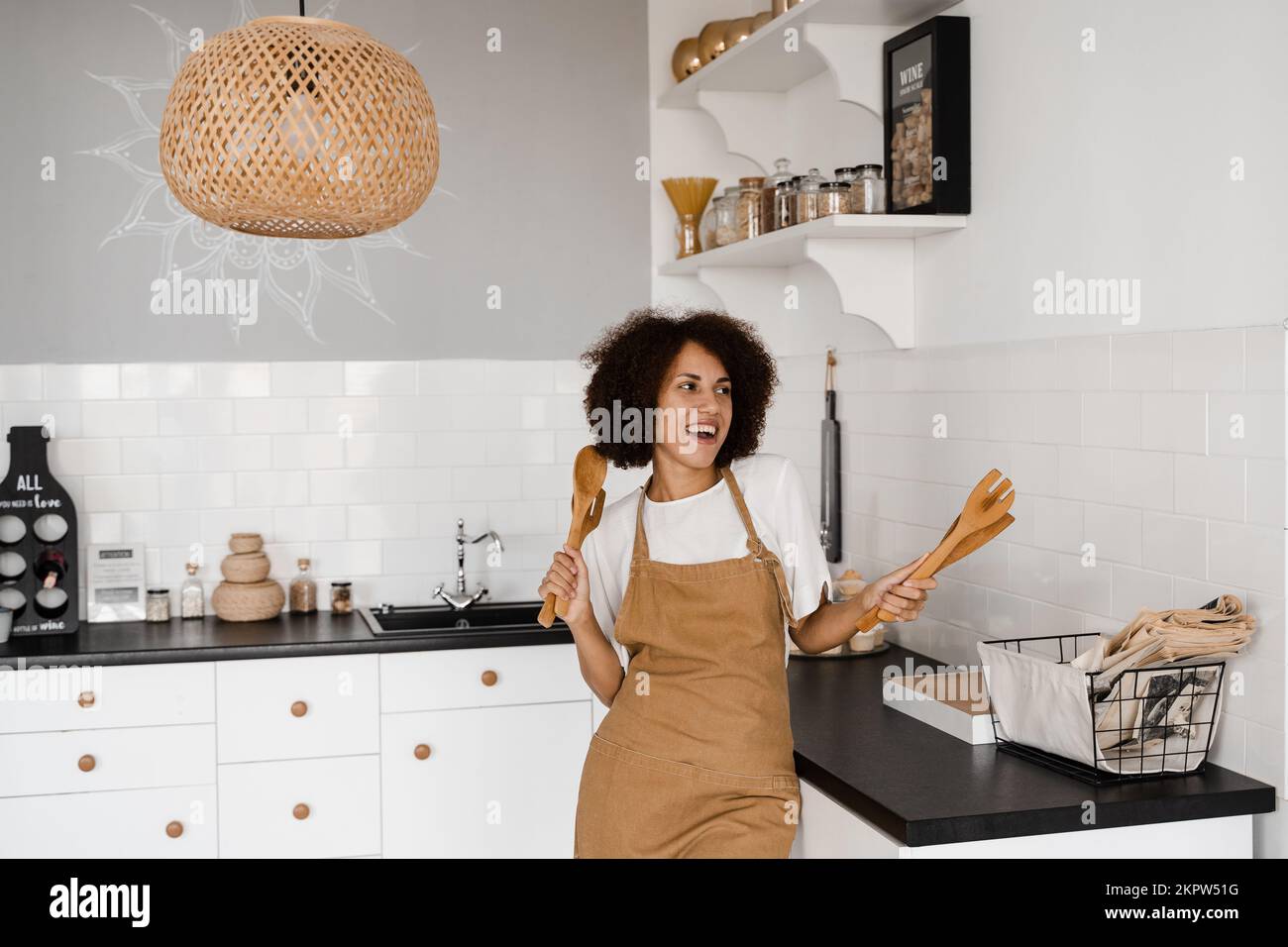 Bonne ménagère africaine en train de chanter et de danser dans la cuisine avant de cuisiner le petit déjeuner. Une jeune fille afro-américaine dansait avec des spatules pour le coo Banque D'Images