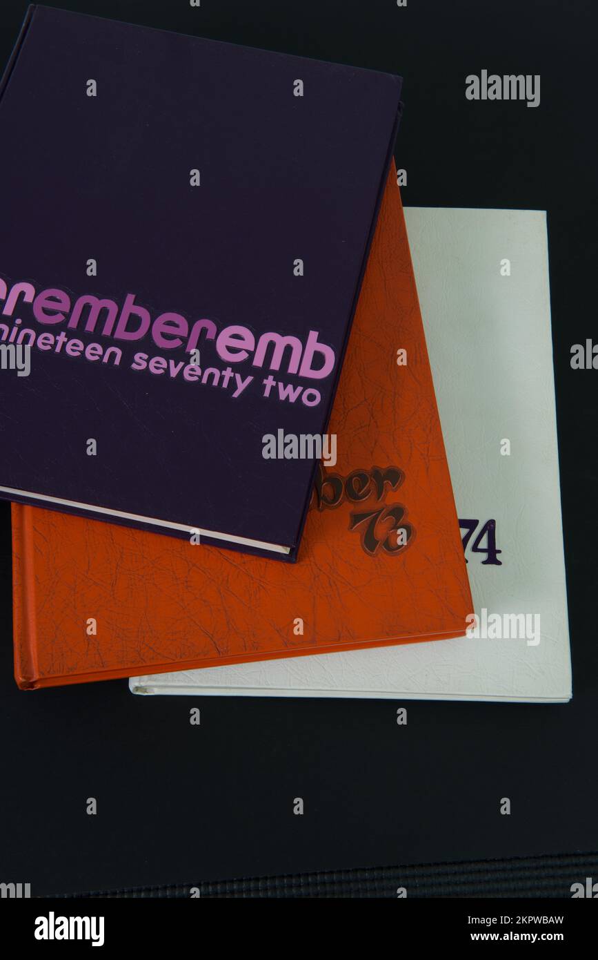Les annuaires d'école secondaire violets, orange et blancs de 1972, 1973 et 1974 sont empilés sur un fond noir. Banque D'Images