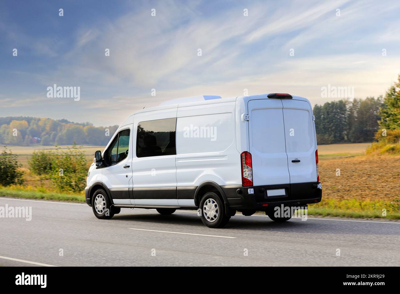 Minibus blanc ou minibus voyageant sur l'autoroute à grande vitesse lors d'une belle journée d'automne, ciel bleu et nuages blancs, vue arrière. Banque D'Images