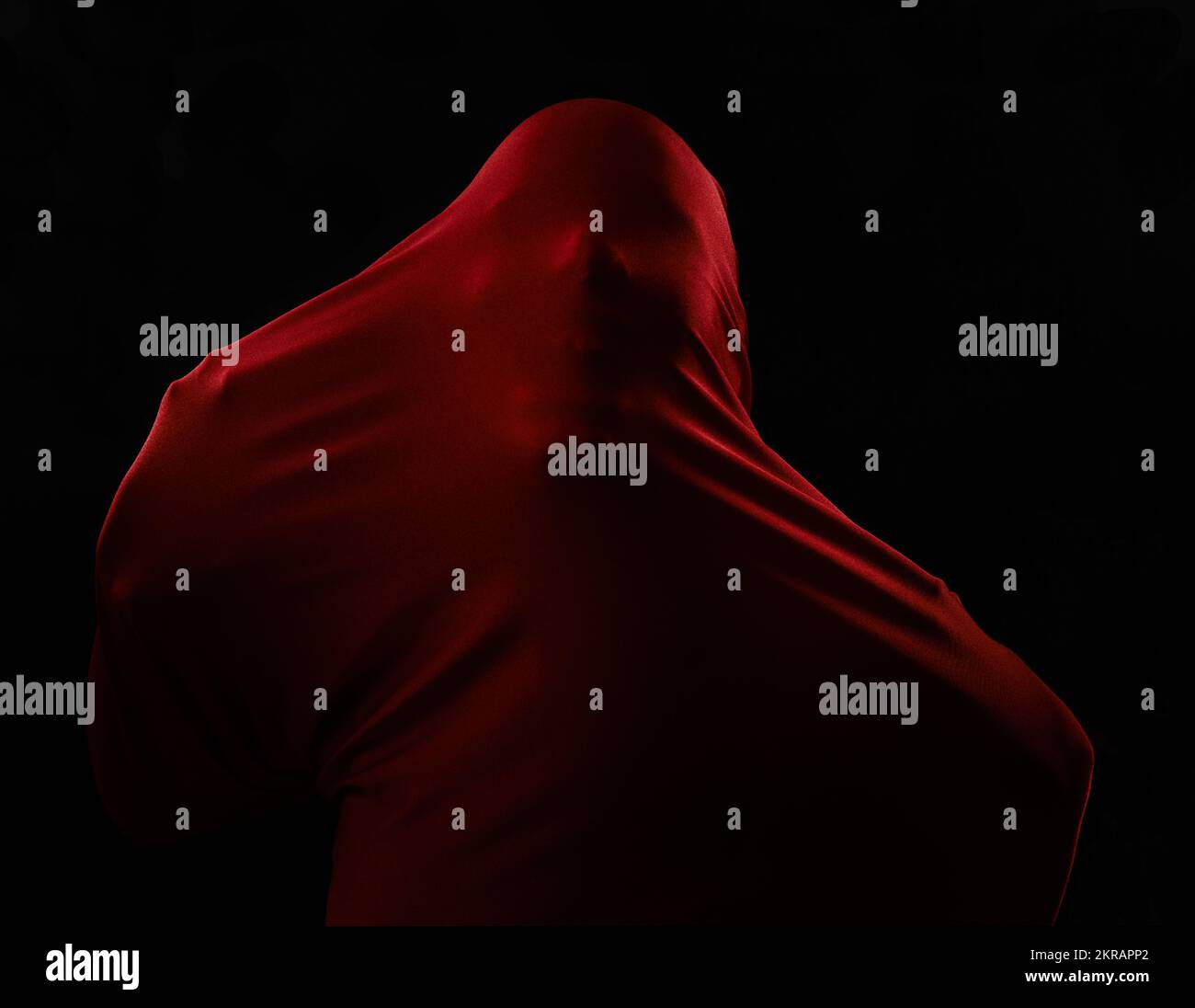 Naissance du mal. Une figure humaine piégée dans un tissu rouge et luttant pour se libérer tout en étant isolée sur le noir. Banque D'Images