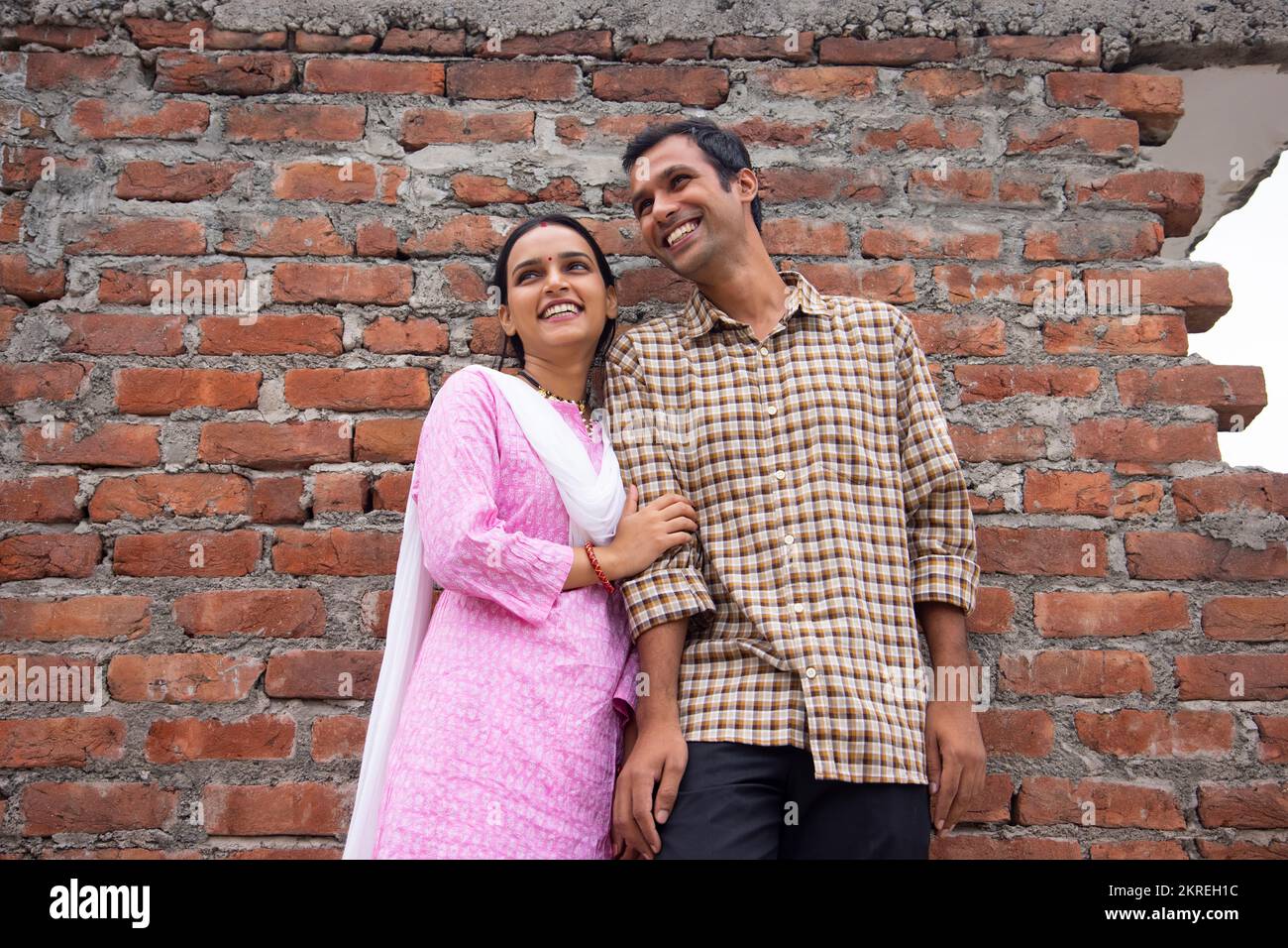 Portrait d'un jeune couple heureux debout contre un mur de briques Banque D'Images