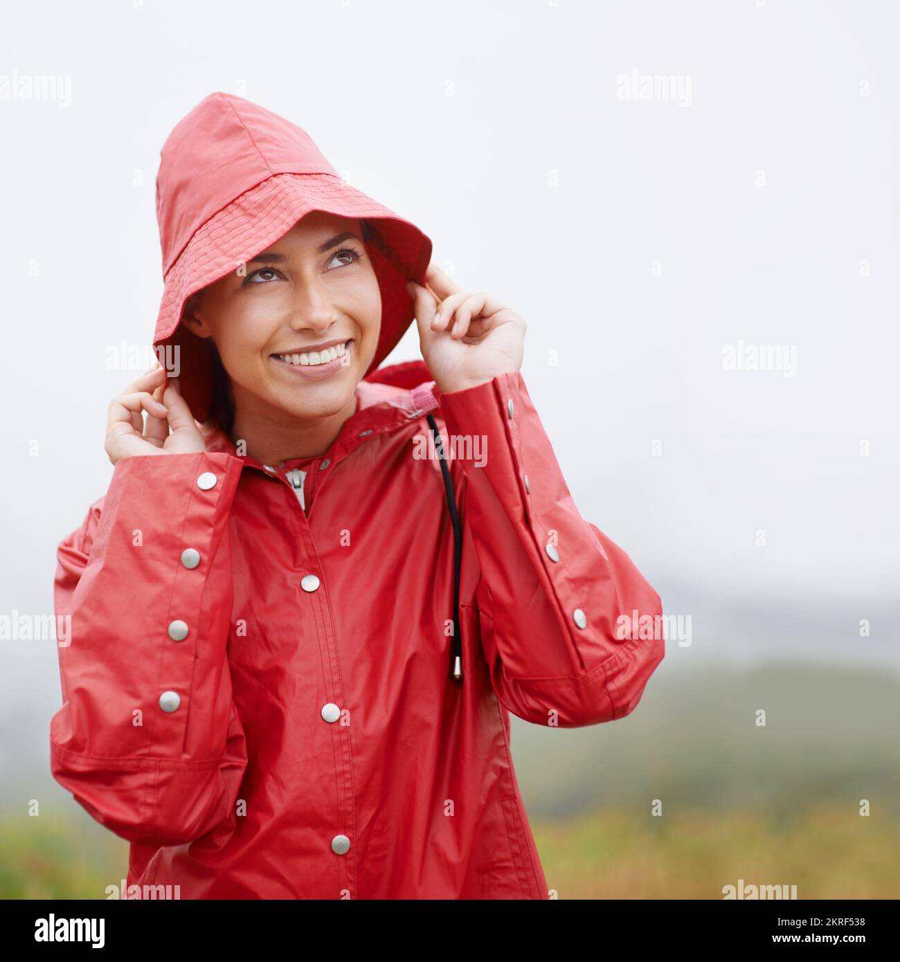 Il semble qu'il pleuve... mais je suis prêt pour ça. une jeune femme attrayante debout sous la pluie. Banque D'Images