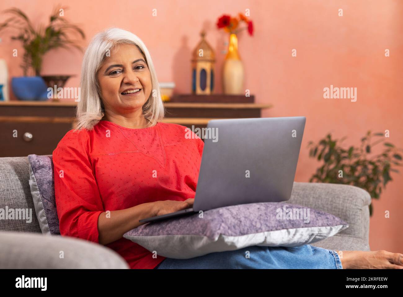 Portrait d'une vieille femme utilisant un ordinateur portable tout en étant assise sur un canapé dans le salon Banque D'Images