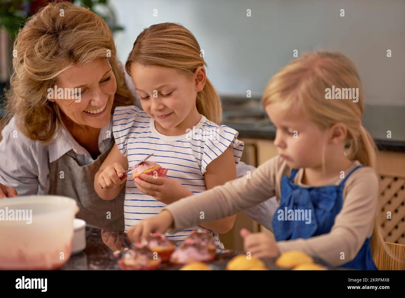 Quand pouvons-nous les manger ? Une grand-mère et ses deux petits-enfants décorent des cupcakes à la maison. Banque D'Images