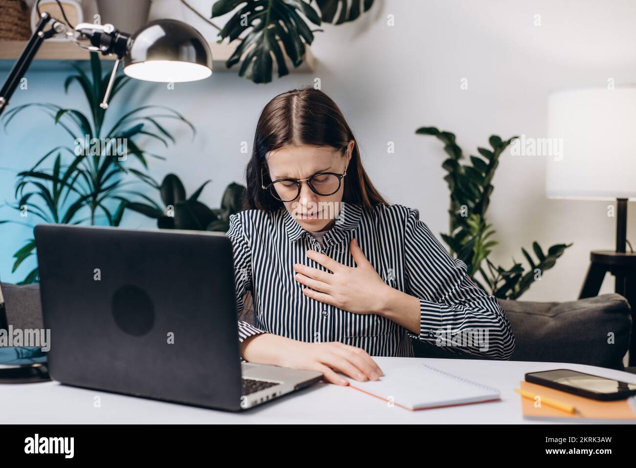 Gros plan de la jeune femme en lunettes travaillant à l'ordinateur, difficulté à respirer ou douleur dans la poitrine touche la poitrine avec la main. Crise de panique, asthme Banque D'Images