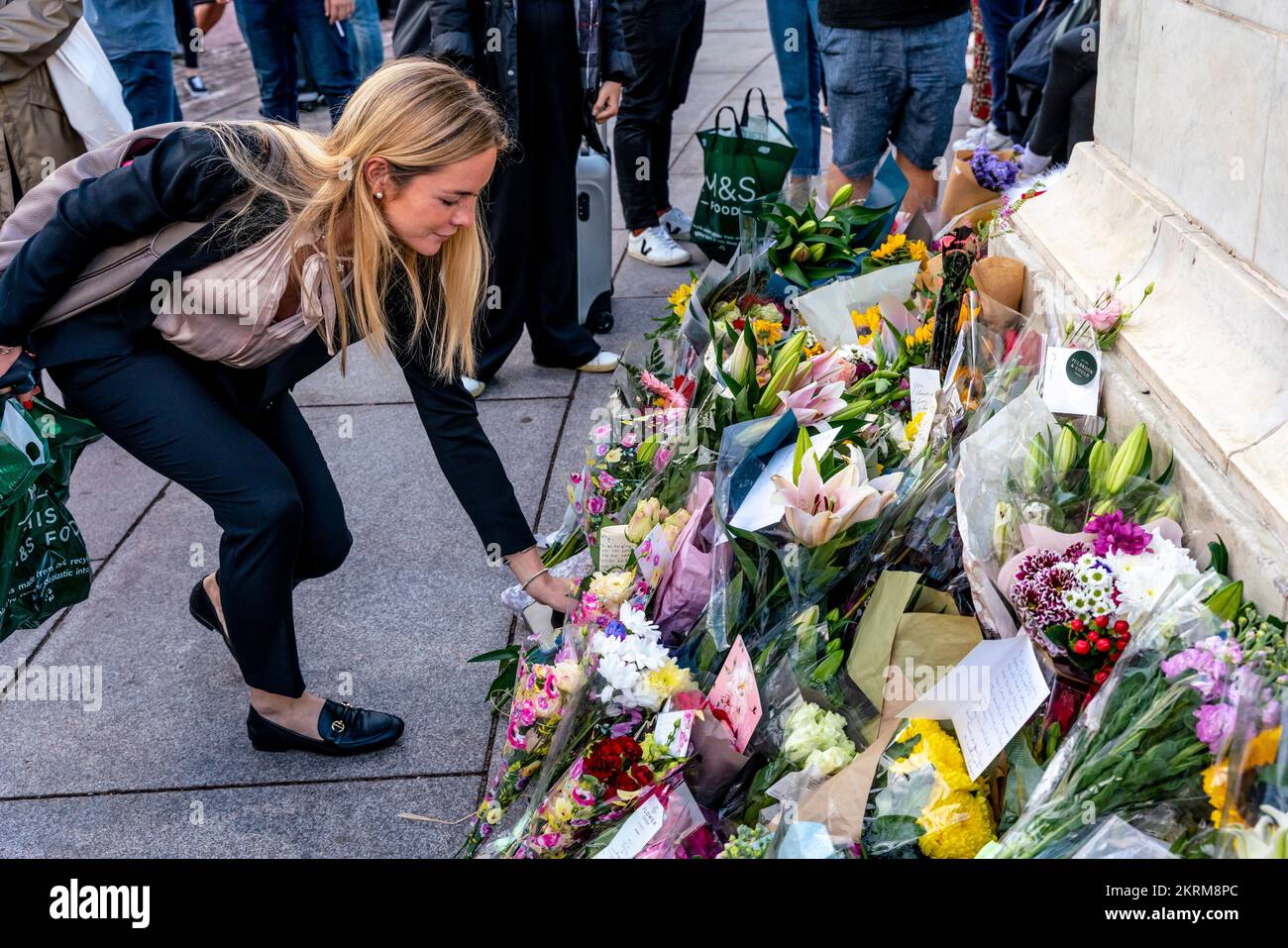 Une jeune femme dépose un hommage floral en face des portes de Buckingham Palace après la mort de la reine Elizabeth II, Londres, Royaume-Uni. Banque D'Images