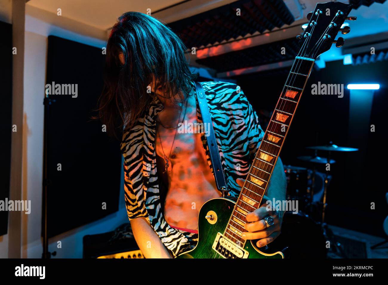 Jeune guitariste aux cheveux longs en lunettes de soleil et chemise rayée jouant de la musique sur guitare électrique pendant la répétition Banque D'Images