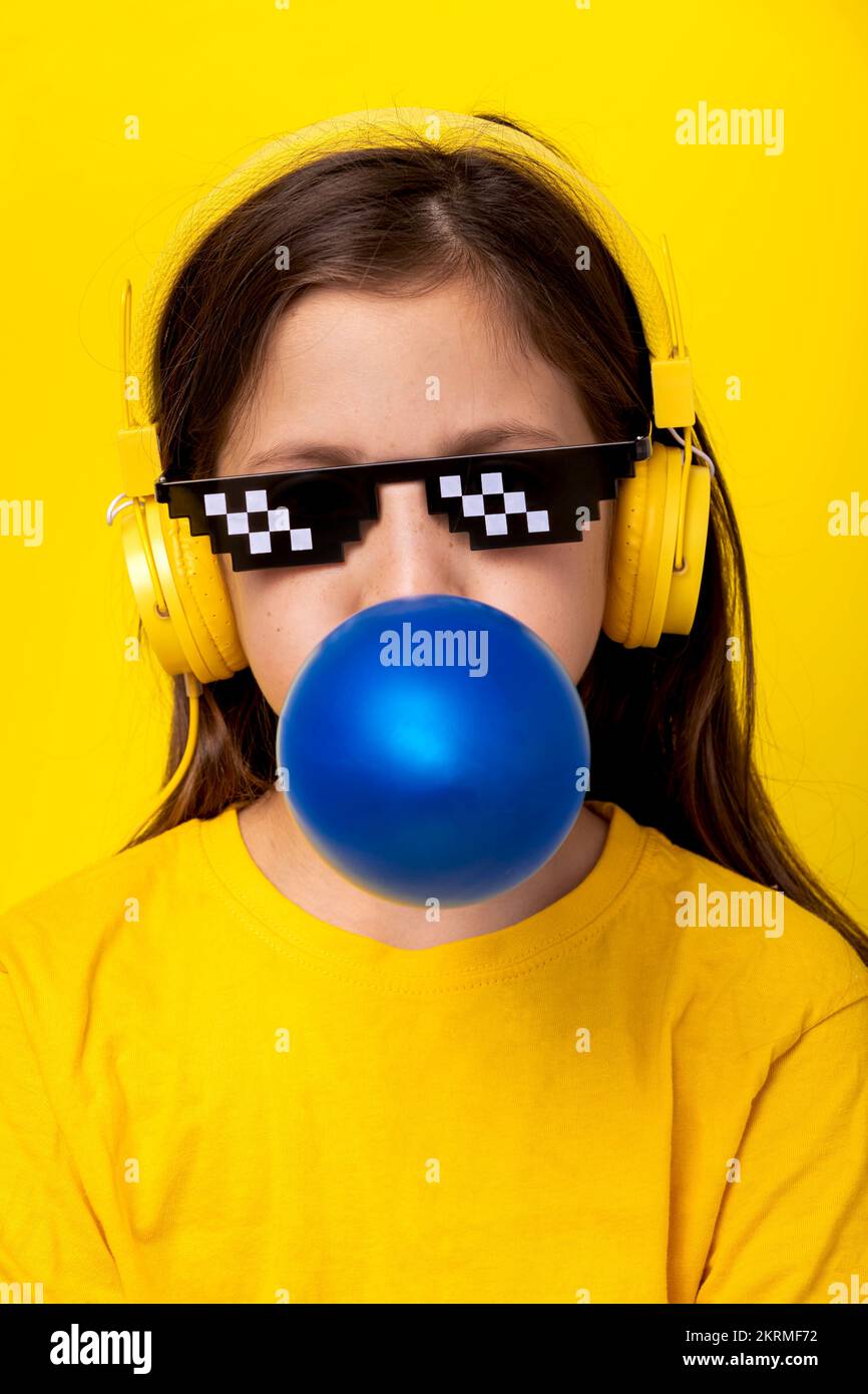 Enfant aux cheveux bruns dans un casque à l'écoute de la musique soufflant  de bulle de gomme bleue tout en se tenant sur fond jaune Photo Stock - Alamy