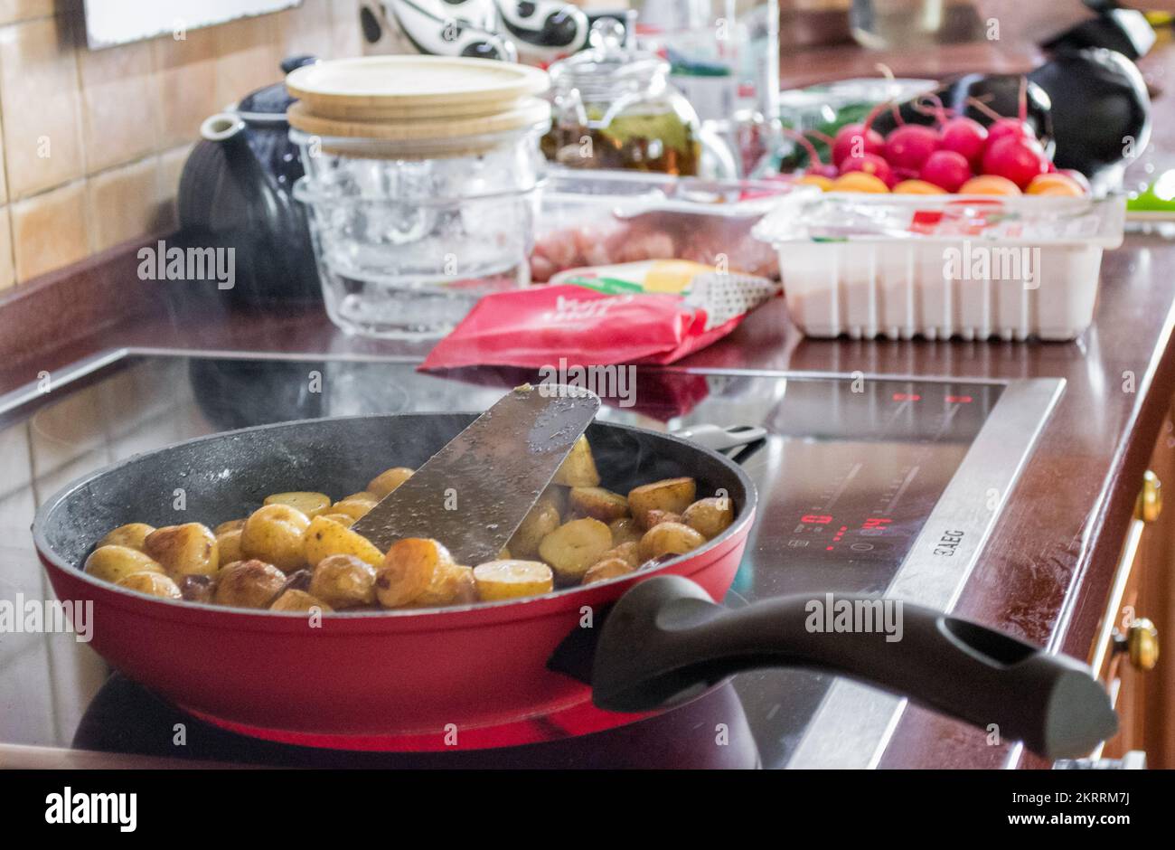 Cuisson à la maison : faire frire de jeunes pommes de terre dans une poêle électrique. Sur fond flou - légumes frais. Banque D'Images